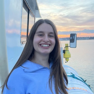Sophie smiling on a boat at sunset, wearing a light blue top.