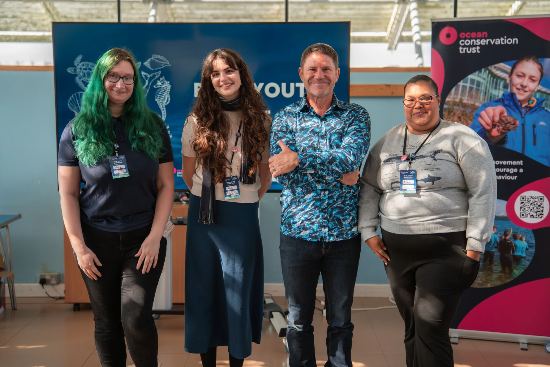 Four people wearing lanyards and smiling beside an Ocean Conservation Trust banner.